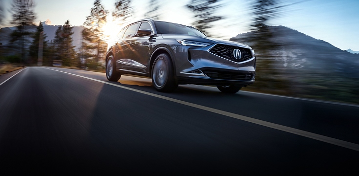 2024 Acura MDX Advance Package in Liquid Carbon Metallic front driving on a scenic road (Premium Performance SUV).