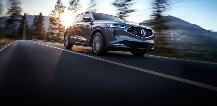 2024 Acura MDX Advance Package in Liquid Carbon Metallic front driving on a scenic road (Premium Performance SUV).