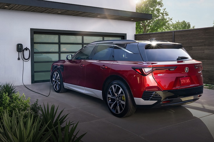 2024 Acura ZDX Type S in Scarlet Red Metallic back charging in a modern driveway (Premium All-Electric SUV).