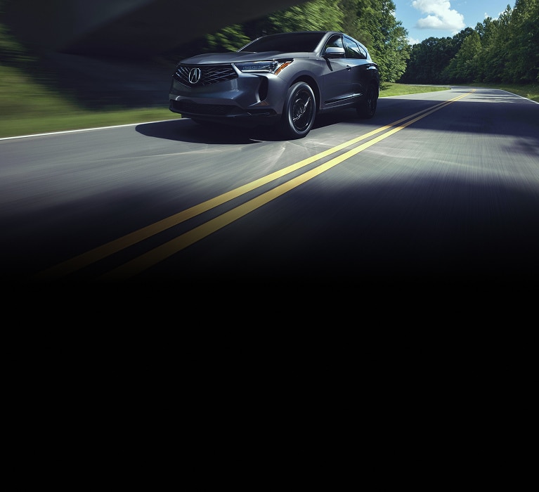 2026 Acura RDX SH-AWD in Liquid Carbon Metallic front driving on a road under an overpass (Premium Sport Crossover SUV). 2026 Acura RDX SH-AWD in Liquid Carbon Metallic front driving on a road under an overpass (Premium Sport Crossover SUV).